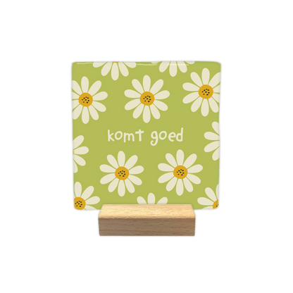 Komt goed - Decoratie tegel - Formaat: - Op deze decoratietegel staat centraal de tekst "komt goed" in kleine, witte letters afgebeeld. De achtergrond heeft een lichtgroene kleur en is bedekt met een patroon van witte bloemen met gele harten. - Snelwenskaart