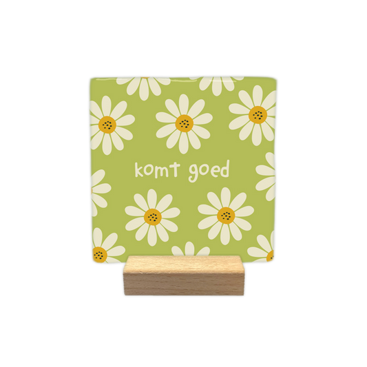 Komt goed - Decoratie tegel - Formaat: - Op deze decoratietegel staat centraal de tekst "komt goed" in kleine, witte letters afgebeeld. De achtergrond heeft een lichtgroene kleur en is bedekt met een patroon van witte bloemen met gele harten. - Snelwenskaart