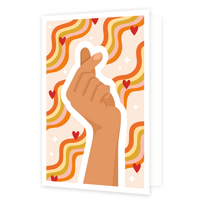 Hartje gebaar vingers - Formaat: Standaard - Vorm: Staand - Blanco kaart - Op deze wenskaart is een hand te zien dat een Koreaans hartje vormt. Op de achtergrond zijn lijnen te zien in de kleuren orangje, geel, goud en roze, samen met rode hartjes. - Snelwenskaart