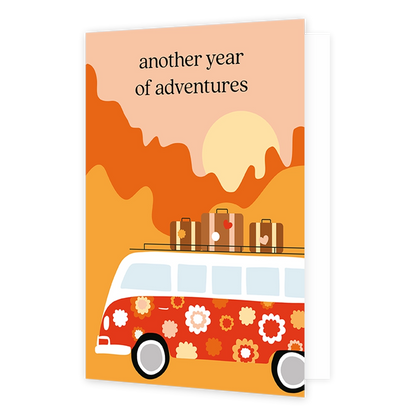 Op deze wenskaart staat een bloemrijke hippie bus met drie koffers op het dak. De kaart is rood, oranje en geel gekleurd. Bovenin de kaart staat de tekst 'another year of adventures'. 