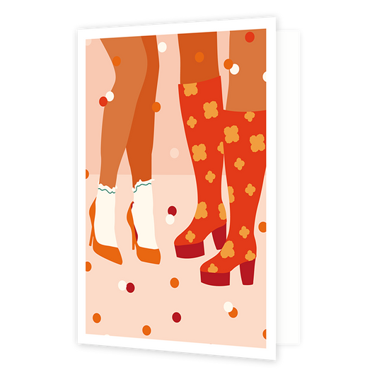 Op deze wenskaart staan twee paar benen. Het ene paar draagt witte sokken in combinatie met lage, oranje hakken. Het andere paar is afgebeeld met hoge rode hakken, voorzien van een oranje bloemmotief.