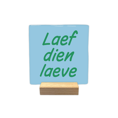 Laef dien laeve - Decoratie tegel - Formaat: - Op deze decoratie tegel staat de tekst "Laef dien laeve" in groene letters. De tekst is verdeeld over drie regels en geplaatst op een lichtblauwe achtergrond. Het gebruikte lettertype is cursief en heeft een vriendelijke, informele uitstraling. - Snelwenskaart