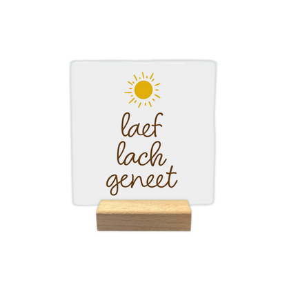 Laef lach geneet - Decoratie tegel - Formaat: - Op deze decoratie tegel staat bovenaan een gestileerde, gele zon met stralen. Daaronder staat in bruine, sierlijke letters de tekst "laef lach geneet" verdeeld over drie regels. Het geheel is geplaatst op een egale witte achtergrond. - Snelwenskaart