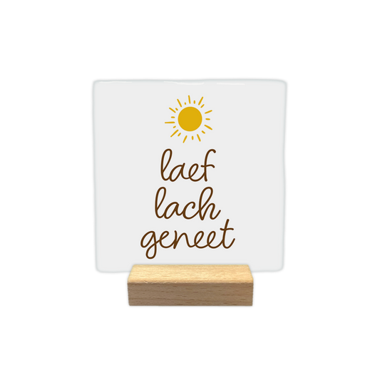 Laef lach geneet - Decoratie tegel - Formaat: - Op deze decoratie tegel staat bovenaan een gestileerde, gele zon met stralen. Daaronder staat in bruine, sierlijke letters de tekst "laef lach geneet" verdeeld over drie regels. Het geheel is geplaatst op een egale witte achtergrond. - Snelwenskaart