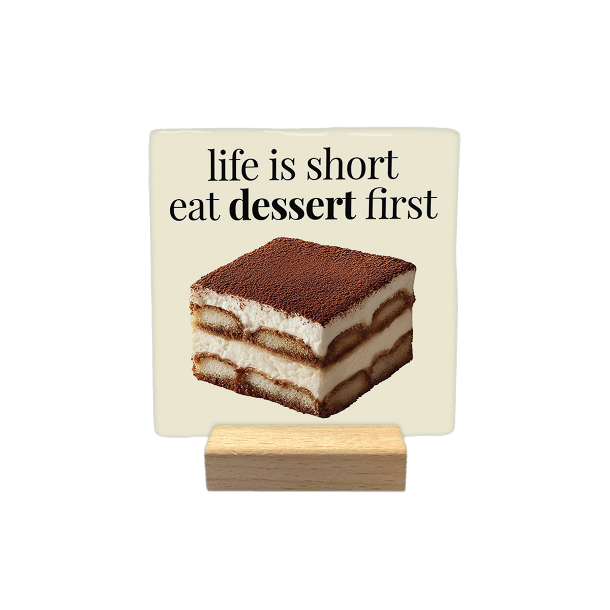 Life is short eat dessert first - Decoratie tegel - Formaat: - Op deze decoratietegel staat de tekst "life is short eat dessert first" in zwarte letters met een schreeflettertype. Daaronder is een realistische afbeelding van een vierkant stuk tiramisu geplaatst. Het ontwerp is gecentreerd op een crèmekleurige achtergrond. - Snelwenskaart