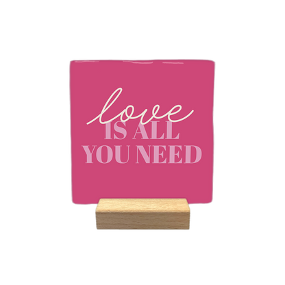 Love is all you need - Decoratie tegel - Formaat: - Op deze decoratietegel staat de tekst "love IS ALL YOU NEED" in een combinatie van sierlijke letters voor het woord "love" en strakke hoofdletters voor de rest. De tekst is in lichtroze uitgevoerd en gecentraliseerd op een donkerroze achtergrond. - Snelwenskaart