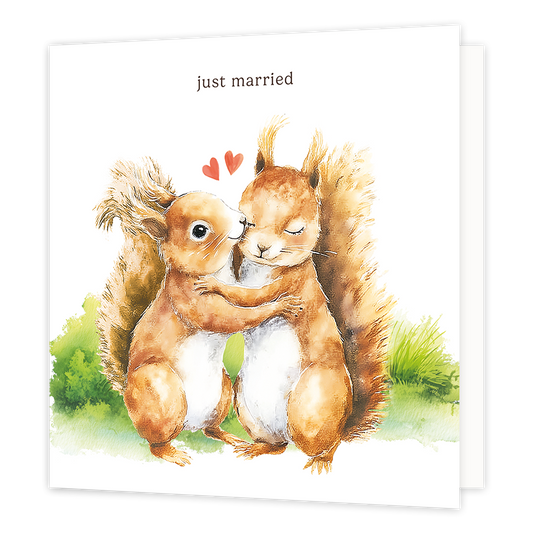 Just married - Formaat: Standaard - Vorm: Vierkant - Huwelijkskaart - Op deze wenskaart staat een aquarelillustratie van twee eekhoorns die elkaar liefdevol omhelzen, waarbij de linker eekhoorn de rechter een kusje geeft. Boven de eekhoorns zweven twee kleine, rode hartjes en bovenaan de illustratie staat de tekst "just married" in donkere letters. De eekhoorns staan afgebeeld op een ondergrond van groen gras tegen een witte achtergrond. - Snelwenskaart