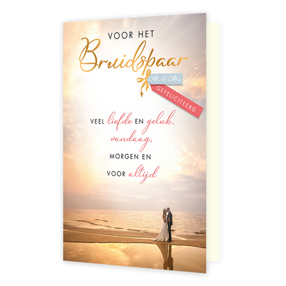 Voor het bruidspaar - Formaat: Standaard - Vorm: Staand - Huwelijkskaart - Op deze wenskaart is een romantisch bruidspaar te zien dat op een strand bij zonsondergang tegenover elkaar staat. Bovenaan de kaart staat de tekst "VOOR HET Bruidspaar" in goudkleurige letters, aangevuld met de tekst "Mr & Mrs" op een blauw label en "GEFELICITEERD" op een roze lint. Centraal op de kaart staat een tekst met gelukswensen die begint met "VEEL liefde EN geluk" en eindigt met "VOOR altijd". De warme kleuren van de zonso