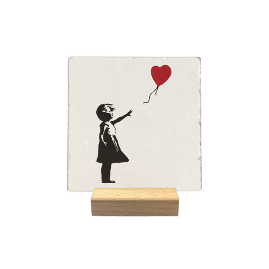 Meisje met ballon - Decoratie tegel - Formaat: - Op deze decoratie tegel staat een zwart silhouet van een jong meisje afgebeeld dat naar rechts kijkt. Ze staat op de grond en reikt met haar uitgestrekte rechterarm naar een rode hartvormige ballon. De ballon zweeft rechts boven haar aan een dun, golvend touwtje. - Snelwenskaart