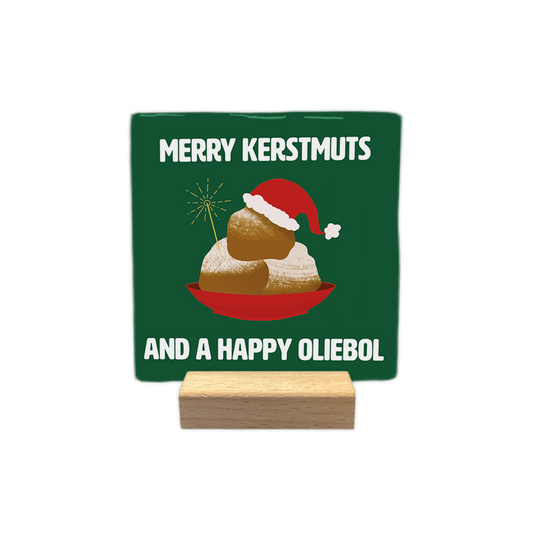 Merry kerstmuts - Decoratie tegel - Formaat: - Op deze decoratie tegel staat een groene achtergrond met een illustratie van een rode schaal met oliebollen erop. De bovenste oliebol draagt een rode kerstmuts met witte rand en er steekt een sterretje uit de schaal. Bovenaan en onderaan staat in witte letters de tekst merry kerstmuts and a happy oliebol. - Snelwenskaart