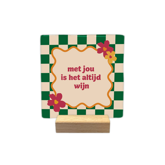 Met jou is het altijd wijn - Decoratie tegel - Formaat: - Op deze decoratie tegel staat de tekst "met jou is het altijd wijn" in roze letters centraal in een crème-kleurig kader met een golvende oranje rand. Het kader is gedecoreerd met bloemen in de hoeken. De achtergrond van de tegel bestaat uit een schaakbordpatroon van donkergroene en crème-kleurige vierkanten. - Snelwenskaart