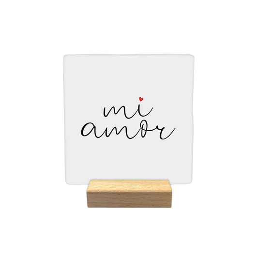 Mi amor - Decoratie tegel - Formaat: - Op deze decoratietegel staat de tekst "mi amor" in een zwart, cursief handschrift. Boven de letter "i" staat een klein, rood hartje. De tekst is gecentreerd op een witte achtergrond. - Snelwenskaart
