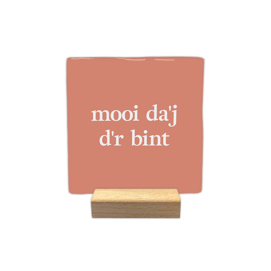 Mooi da'j d'r bint - Decoratie tegel - Formaat: - Op deze decoratie tegel staat de tekst "mooi da'j d'r bint" in witte letters verdeeld over twee regels. De achtergrond heeft een egale, zalmroze kleur. Het ontwerp is rustig en minimalistisch vormgegeven. - Snelwenskaart