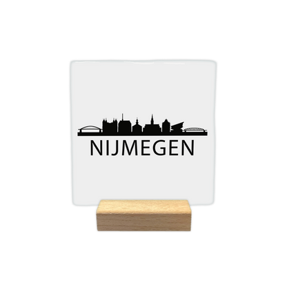 Nijmegen skyline - Decoratie tegel - Formaat: - Op deze decoratie tegel staat bovenaan een zwart silhouet van de stad Nijmegen, inclusief de Waalbrug en verschillende bekende gebouwen. Daaronder staat in grote, zwarte letters de tekst "nijmegen". Het gehele ontwerp is afgebeeld op een witte achtergrond. - Snelwenskaart