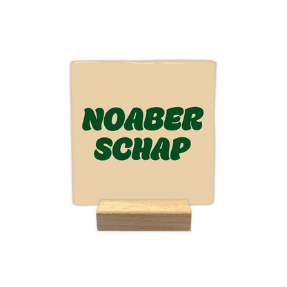 Noaberschap - Decoratie tegel - Formaat: - Op deze decoratie tegel staat de tekst "noaber schap" in donkergroene, golvende letters verdeeld over twee regels. Het ontwerp is geplaatst op een egale, lichtbeige achtergrond. - Snelwenskaart