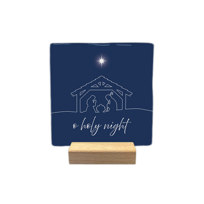 O holy night - Decoratie tegel - Formaat: - Op deze decoratie tegel staat een donkerblauwe achtergrond. In het midden is met witte lijnen een kerststal afgebeeld, met daarin de silhouetten van Maria, Jozef en het kindje Jezus in een kribbe. Boven de stal schittert een witte ster. Onderaan staat in witte sierletters de tekst o holy night. - Snelwenskaart