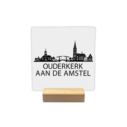 Ouderkerk aan de Amstel skyline - Decoratie tegel - Formaat: - Op deze decoratie tegel staat een zwarte skyline van Ouderkerk aan de Amstel op een witte achtergrond. Het ontwerp toont diverse kenmerkende gebouwen, waaronder een kerk en een ophaalbrug. Onder de skyline staat in zwarte letters de plaatsnaam Ouderkerk aan de Amstel. De illustratie is volledig in zwart en wit uitgevoerd. - Snelwenskaart