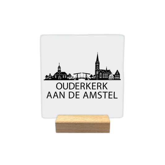 Ouderkerk aan de Amstel skyline - Decoratie tegel - Formaat: - Op deze decoratie tegel staat een zwarte skyline van Ouderkerk aan de Amstel op een witte achtergrond. Het ontwerp toont diverse kenmerkende gebouwen, waaronder een kerk en een ophaalbrug. Onder de skyline staat in zwarte letters de plaatsnaam Ouderkerk aan de Amstel. De illustratie is volledig in zwart en wit uitgevoerd. - Snelwenskaart