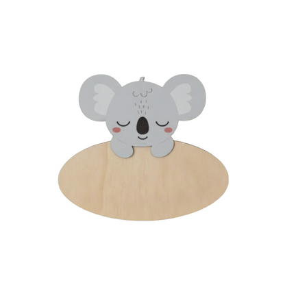 Dit naambord is voorzien van een schattige, slapende koala in grijstinten met grote, ronde oren en rode blosjes op de wangen. De koala steunt met twee pootjes over de bovenkant van een ovaal houten bord heen.
