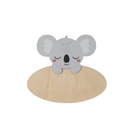 Dit naambord is voorzien van een schattige, slapende koala in grijstinten met grote, ronde oren en rode blosjes op de wangen. De koala steunt met twee pootjes over de bovenkant van een ovaal houten bord heen.