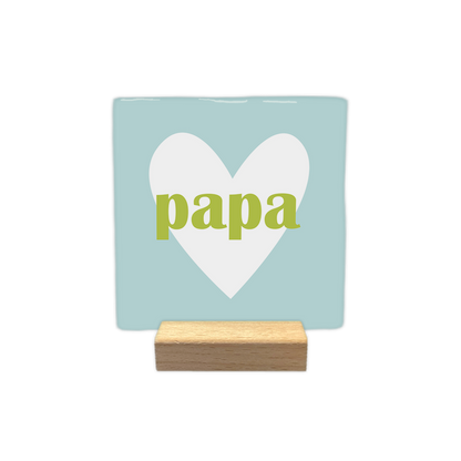 Papa - Decoratie tegel - Formaat: - Op deze decoratie tegel staat centraal een groot wit hart afgebeeld tegen een lichtblauwe achtergrond. In het midden van dit hart is het woord "papa" in kleine, groene letters geplaatst. Het ontwerp is eenvoudig en rustig van uitstraling. - Snelwenskaart