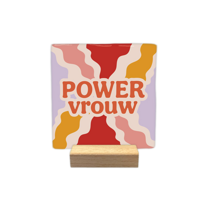 Power vrouw - Decoratie tegel - Formaat: 10 x 10 cm -  Op deze decoratietegel staat in het midden de Nederlandse tekst "POWER vrouw". De tegel zelf is vierkant, staat in een houten standaard en heeft een retro achtergrond met golvende stralen in de kleuren rood, okergeel, roze en lila. De tekst is verdeeld over twee regels en is geschreven in dikke, oranje letters met een brede, beige omlijning. Het woord "POWER" staat volledig in hoofdletters, terwijl "vrouw" in kleine letters is geschreven - Snelwenskaart