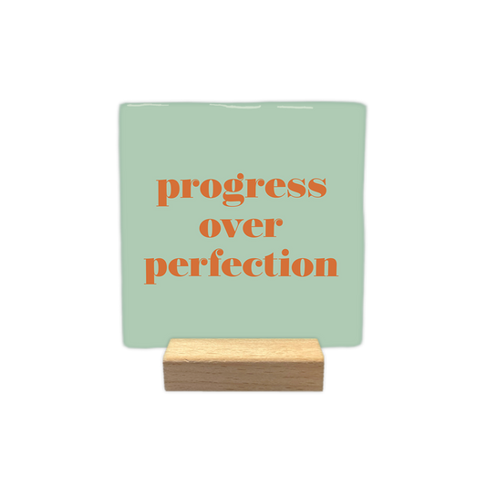 Progress over perfection - Decoratie tegel - Formaat: - Op deze decoratietegel staat de tekst "progress over perfection" in kleine letters met een schreeflettertype. De tekst is uitgevoerd in een oranje kleur en is gecentreerd op een mintgroene achtergrond. - Snelwenskaart