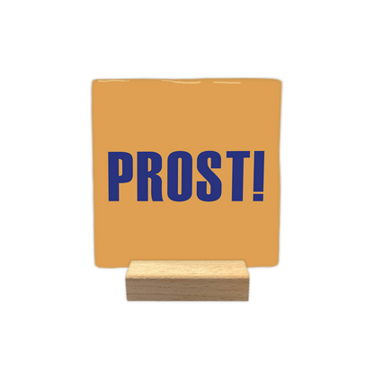 Prost! - Decoratie tegel - Formaat: - Op deze decoratie tegel staat het woord "prost!" afgebeeld in blauwe letters. De achtergrond van de tegel is oranje van kleur. - Snelwenskaart