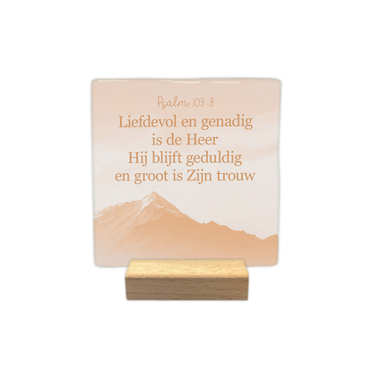 Psalm 103:8 - Decoratie tegel - Formaat: - Op deze decoratie tegel staat bovenaan de tekst "Psalm 103:8" met daaronder de bijbeltekst "Liefdevol en genadig is de Heer, Hij blijft geduldig en groot is Zijn trouw". De tekst is weergegeven in een bruine kleur. Op de achtergrond is een bergzicht afgebeeld in zachte, oranjeachtige tinten. Het ontwerp heeft een rustige en serene uitstraling. - Snelwenskaart