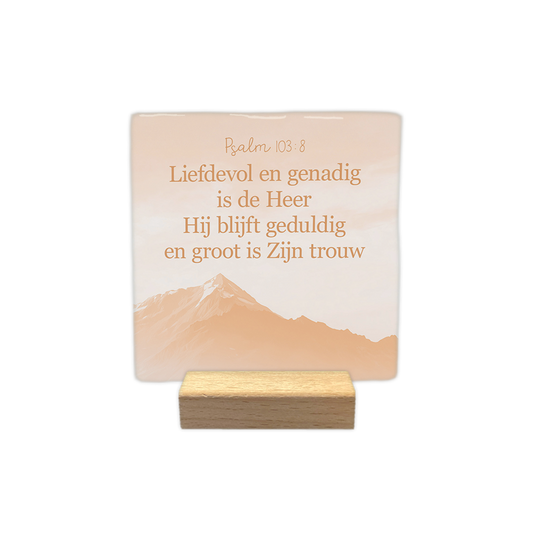 Psalm 103:8 - Decoratie tegel - Formaat: - Op deze decoratie tegel staat bovenaan de tekst "Psalm 103:8" met daaronder de bijbeltekst "Liefdevol en genadig is de Heer, Hij blijft geduldig en groot is Zijn trouw". De tekst is weergegeven in een bruine kleur. Op de achtergrond is een bergzicht afgebeeld in zachte, oranjeachtige tinten. Het ontwerp heeft een rustige en serene uitstraling. - Snelwenskaart