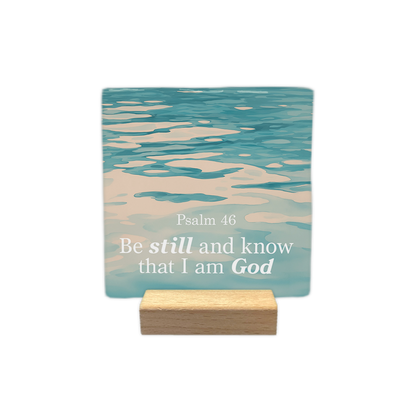 Psalm 46 - Decoratie tegel - Formaat: - Op deze decoratie tegel staat de tekst "Psalm 46" met daaronder "Be still and know that I am God" in witte letters. De woorden "still" en "God" zijn daarbij in een andere stijl weergegeven. De achtergrond toont een foto van kabbelend, blauwachtig water. - Snelwenskaart