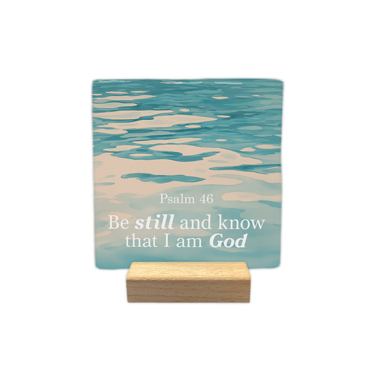 Psalm 46 - Decoratie tegel - Formaat: - Op deze decoratie tegel staat de tekst "Psalm 46" met daaronder "Be still and know that I am God" in witte letters. De woorden "still" en "God" zijn daarbij in een andere stijl weergegeven. De achtergrond toont een foto van kabbelend, blauwachtig water. - Snelwenskaart