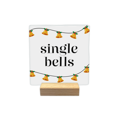 Single bells - Decoratie tegel - Formaat: - Op deze decoratie tegel staat een witte achtergrond. Aan de boven- en onderkant loopt een zwarte lijn met daaraan hangende gouden klokjes en groene blaadjes met rode bessen. In het midden staat in zwarte letters de tekst single bells. - Snelwenskaart