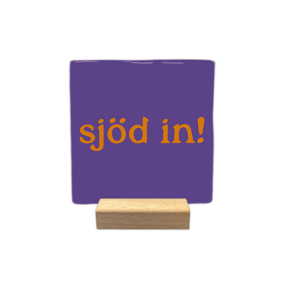 Sjöd in! - Decoratie tegel - Formaat: - Op deze decoratie tegel staat de oranje tekst "sjöd in!" centraal afgebeeld tegen een paarse achtergrond. Het ontwerp is eenvoudig en strak vormgegeven. - Snelwenskaart