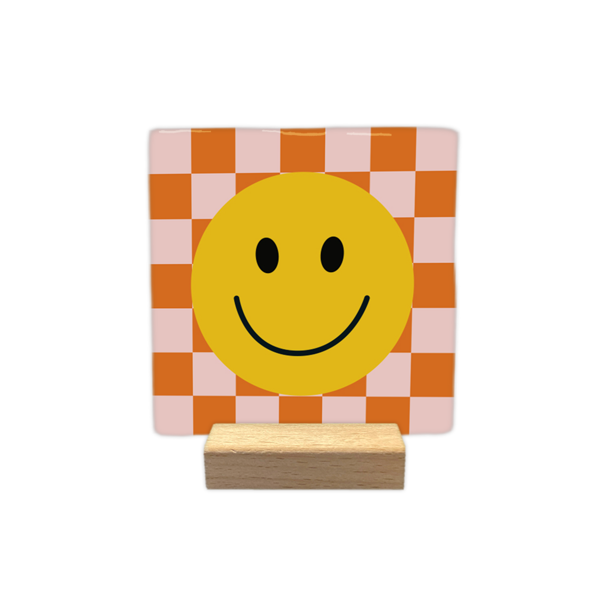 Smiley - Decoratie tegel - Formaat: - Op deze decoratietegel staat centraal een grote, gele smiley afgebeeld met zwarte ogen en een glimlachende mond. De achtergrond van de illustratie bestaat uit een schaakbordpatroon van afwisselend oranje en lichtroze vierkanten. - Snelwenskaart
