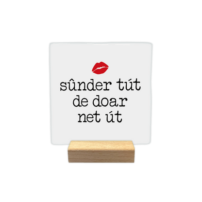 Sûnder tút de doar net út - Decoratie tegel - Formaat: - Op deze decoratie tegel staat de tekst "sûnder tút de doar net út" in zwarte letters centraal afgebeeld, zoals te zien is in RTK456.jpg. Boven de tekst bevindt zich een afbeelding van rode lippen. De achtergrond van de tegel is wit. - Snelwenskaart