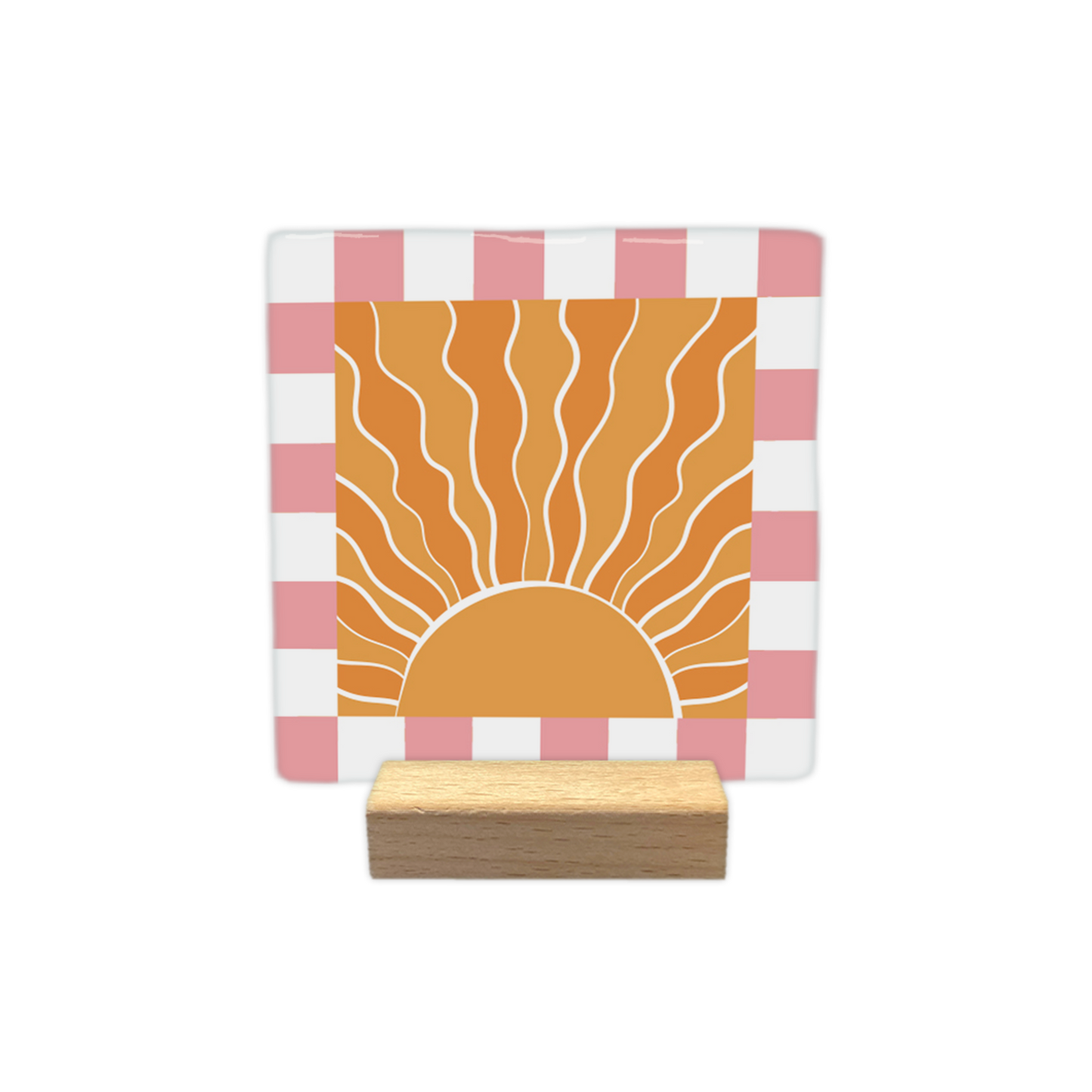 Sunshine - Decoratie tegel - Formaat: - Op deze decoratietegel staat een gestileerde, opkomende zon centraal afgebeeld in een oranje vierkant. De zon is getekend met golvende, witte stralen die naar boven uitstralen vanuit een halve cirkel aan de onderzijde. Het centrale oranje vierkant is omgeven door een rand met een schaakbordpatroon van afwisselende witte en roze vierkanten. - Snelwenskaart