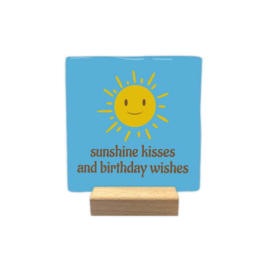 Sunshine kisses and birthday wishes - Decoratie tegel - Formaat: - Op deze decoratie tegel staat in het bruin de tekst 'Sunshine kisses and birthday wishes'. Boven de tekst staat een gele zon met gezicht. De achtergrond van de decoratie tegel is blauw. - Snelwenskaart