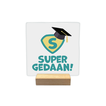 Super gedaan! - Decoratie tegel - Formaat: - Op deze decoratie tegel staat een geel en groen superman logo met een afstudeerhoed erop. Onder het logo staat in het groen de tekst 'Super gedaan!'. - Snelwenskaart