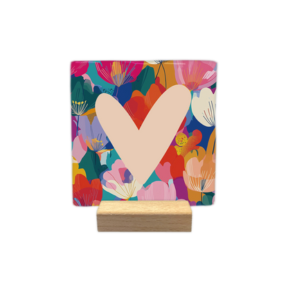 Decoratietegel – 10 x 10 cm - Op deze decoratietegel staat centraal een groot, lichtbeige hart tegen een kleurrijke achtergrond die is opgebouwd uit een abstract patroon van gestileerde bloemen en bladeren in tinten als roze, rood, geel, oranje en diepblauw.