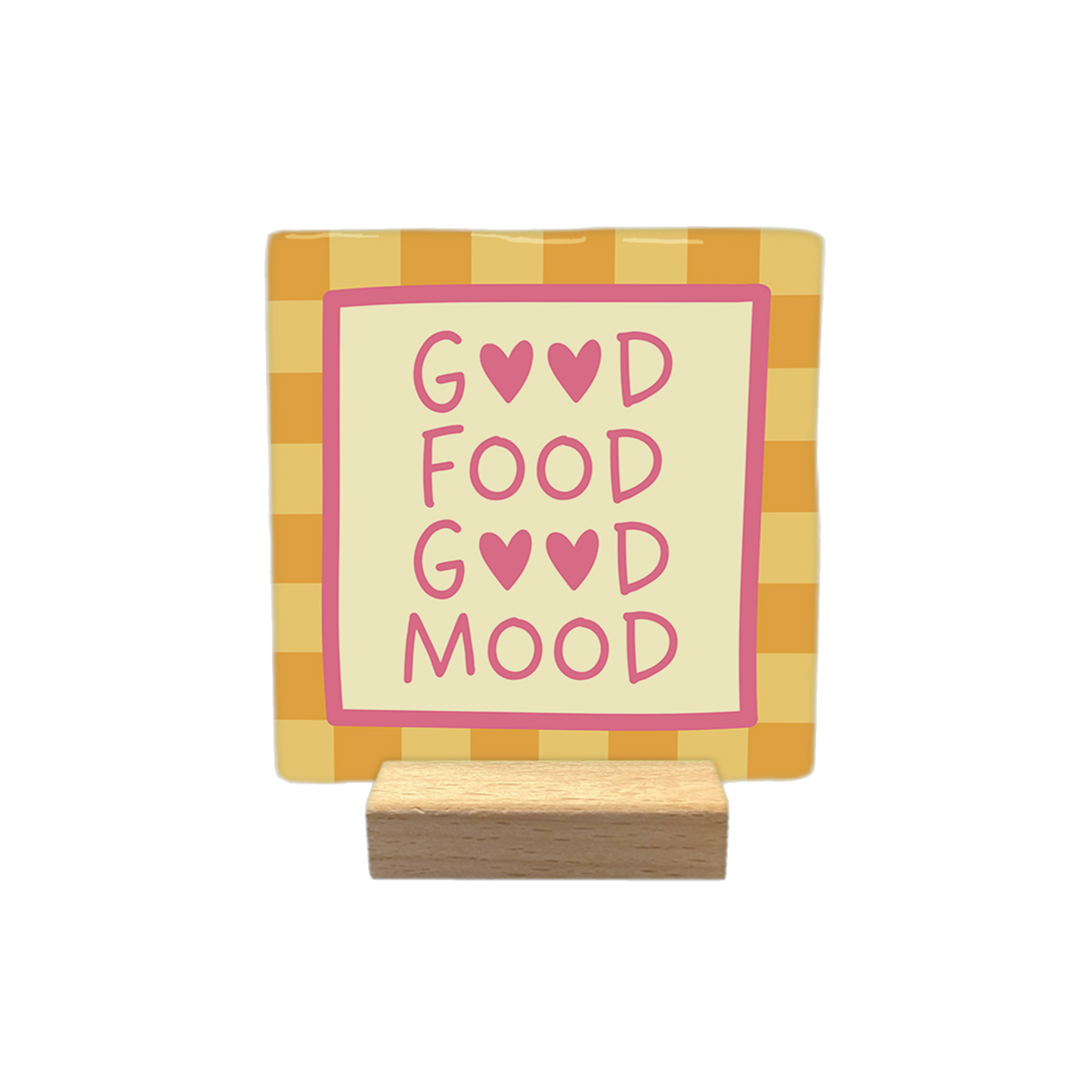 Decoratietegel – 10 x 10 cm - Op deze decoratietegel staat de tekst "GOOD FOOD GOOD MOOD" in roze letters, waarbij de letter 'O' in de woorden 'GOOD' is vervangen door roze hartjes. De tekst is geplaatst op een crèmekleurig middenveld dat wordt omlijst door een roze rand. De achtergrond van de tegel heeft een oranje-geel ruitpatroon.