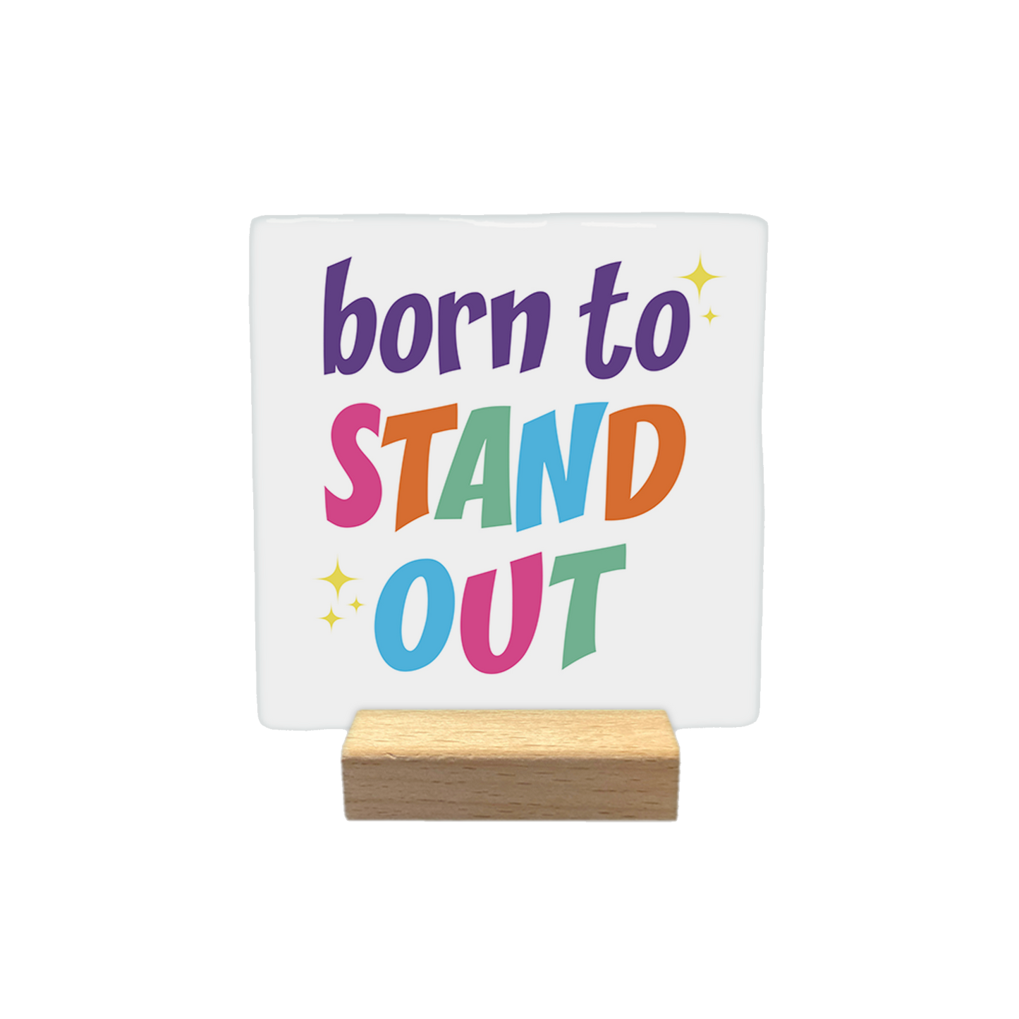 Decoratietegel – 10 x 10 cm - Op deze decoratietegel staat de tekst "born to STAND OUT" in een kleurrijke en speelse typografie. De woorden "STAND" en "OUT" zijn elk opgebouwd uit letters in verschillende kleuren, en het ontwerp is verfraaid met kleine, gele sterretjes.