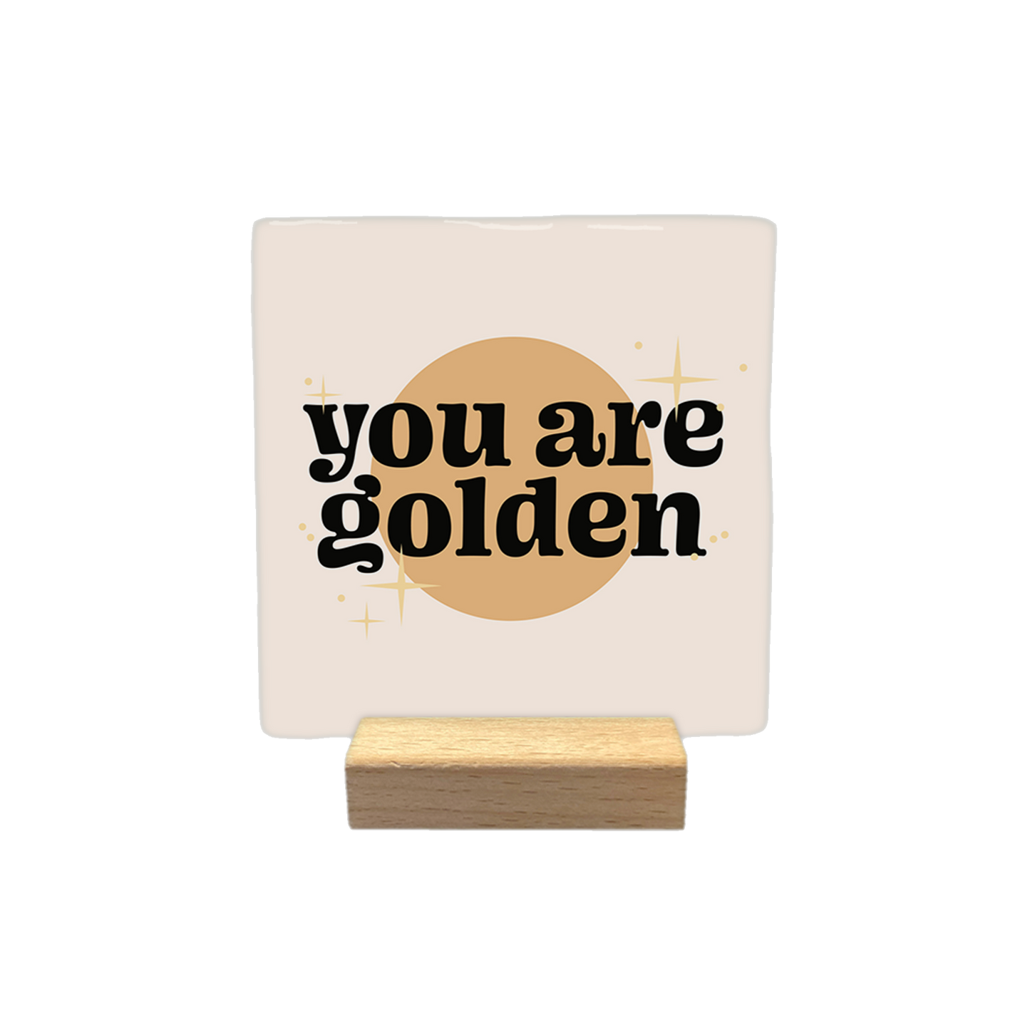 Decoratietegel – 10 x 10 cm - Op deze decoratietegel staat de tekst "you are golden" in zwarte letters met een afgerond, speels lettertype. De tekst is gecentreerd over een goudkleurige cirkel en wordt omringd door kleine, gestileerde sterretjes. Het gehele ontwerp bevindt zich op een crèmekleurige achtergrond.