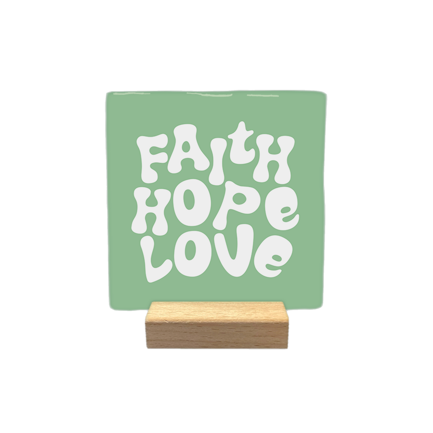 Decoratietegel – 10 x 10 cm - Op deze decoratietegel staat de tekst "FAITH HOPE LOVE" in witte letters met een speels, golvend lettertype. De tekst is gecentreerd op een groene, vierkante achtergrond.