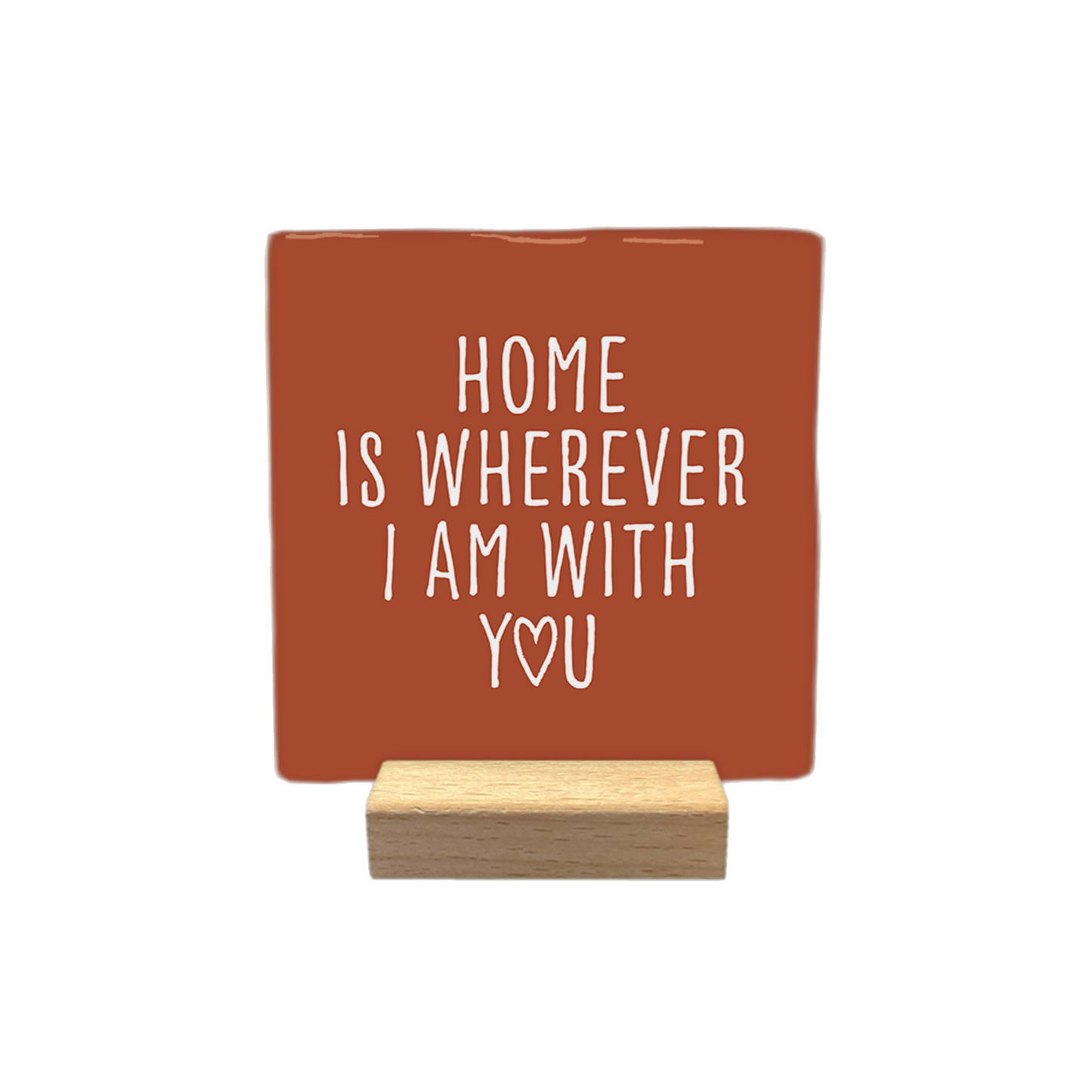 Decoratietegel – 10 x 10 cm - Op deze decoratietegel staat de tekst "HOME IS WHEREVER I AM WITH YOU" in witte letters met een strak, handgeschreven lettertype. De letter "O" in het woord "YOU" is vervangen door een hartje. De tekst is gecentreerd op een roodbruine achtergrond.