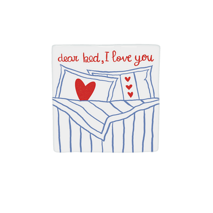 Decoratietegel – 10 x 10 cm - Op deze decoratietegel staat bovenaan de tekst "dear bed, I love you" in een handgeschreven rood lettertype. Daaronder is een illustratie afgebeeld van een opgemaakt bed met blauw-witte strepen, voorzien van kussens die zijn versierd met rode hartjes. Het ontwerp is gecentreerd op een witte achtergrond. 