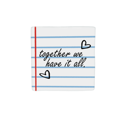 Decoratietegel – 10 x 10 cm - Op deze decoratietegel staat de tekst "together we have it all." in een zwart, cursief lettertype. De achtergrond heeft het uiterlijk van gelinieerd schriftpapier met blauwe horizontale lijnen en een rode verticale kantlijn. Het ontwerp wordt aangevuld met twee handgetekende zwarte hartjes. Iedere tegel wordt geleverd inclusief houten presentatieblok. 