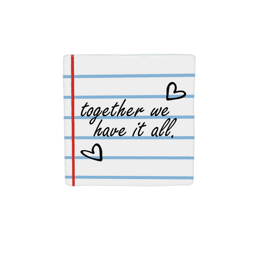 Decoratietegel – 10 x 10 cm - Op deze decoratietegel staat de tekst "together we have it all." in een zwart, cursief lettertype. De achtergrond heeft het uiterlijk van gelinieerd schriftpapier met blauwe horizontale lijnen en een rode verticale kantlijn. Het ontwerp wordt aangevuld met twee handgetekende zwarte hartjes. Iedere tegel wordt geleverd inclusief houten presentatieblok. 