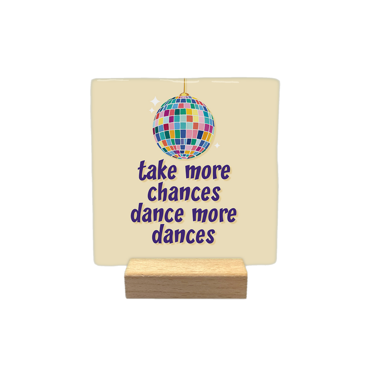 Take more chances dance more dances - Decoratie tegel - Formaat: - Op deze decoratietegel staat een afbeelding van een kleurrijke discobal boven de tekst "take more chances dance more dances" in paarse letters. De tekst en de discobal zijn gecentreerd op een lichtbeige achtergrond. - Snelwenskaart