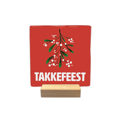 Takkefeest - Decoratie tegel - Formaat: - Op deze decoratie tegel staat een rode achtergrond met een illustratie van een takje maretak met groene bladeren en witte bessen. Onder de maretak staat in grote witte letters de tekst takkefeest. - Snelwenskaart
